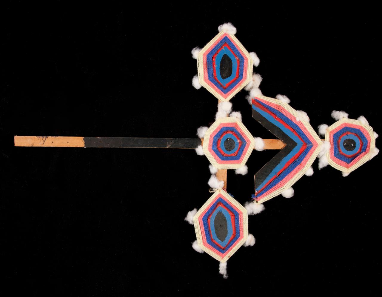 A ceremonial wooden object in the shape of an arrow painted pink, purple and white