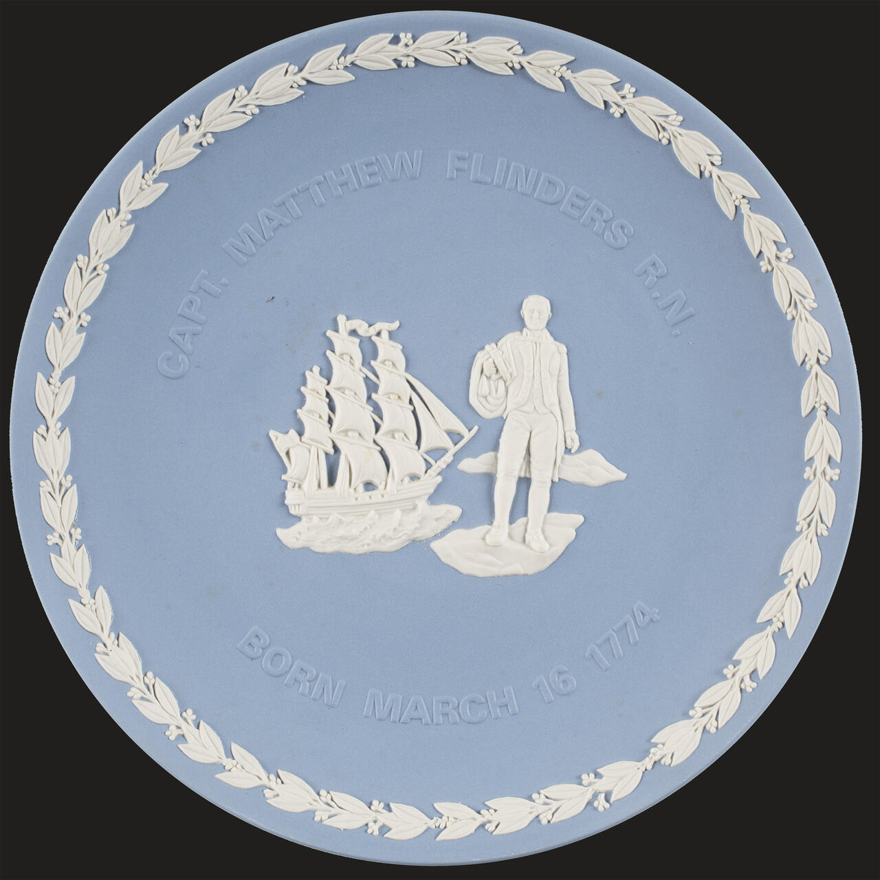 blue plate featuring a white boarder and image of a man standing in front of a sailing ship. 